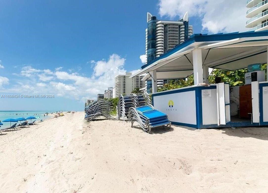 A beachside cabana with stacked lounge chairs sits on the sand near high-rise buildings — 6365 Collins Ave # 4209, Miami Beach FL 33141, MIAMI BEACH, FL