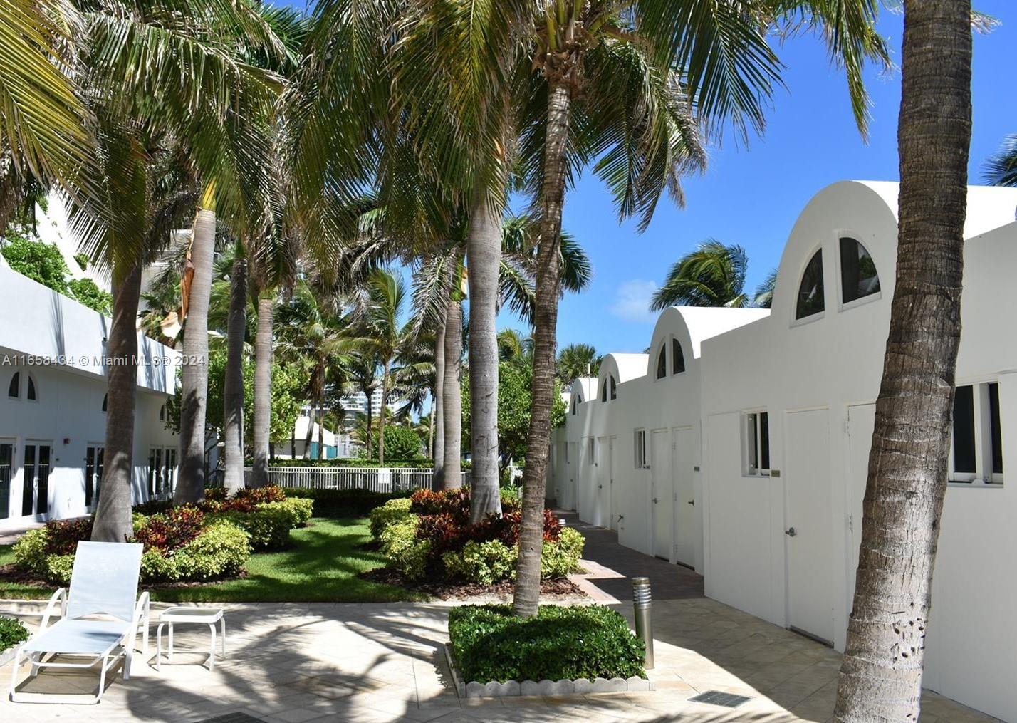 A courtyard with palm trees, white arched buildings, and a lounge chair on a patio — 6365 Collins Ave # 4209, Miami Beach FL 33141, MIAMI BEACH, FL