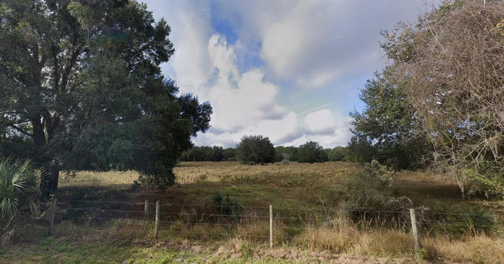 A wire fence borders a grassy, open field surrounded by mature trees under a cloudy sky — 00 SE 34TH WAY, SUMTERVILLE, FL