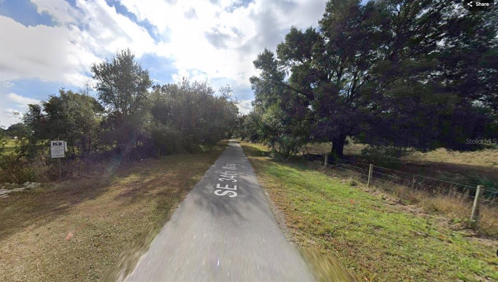 A paved path runs through a grassy area lined with trees and a wire fence — 00 SE 34TH WAY, SUMTERVILLE, FL