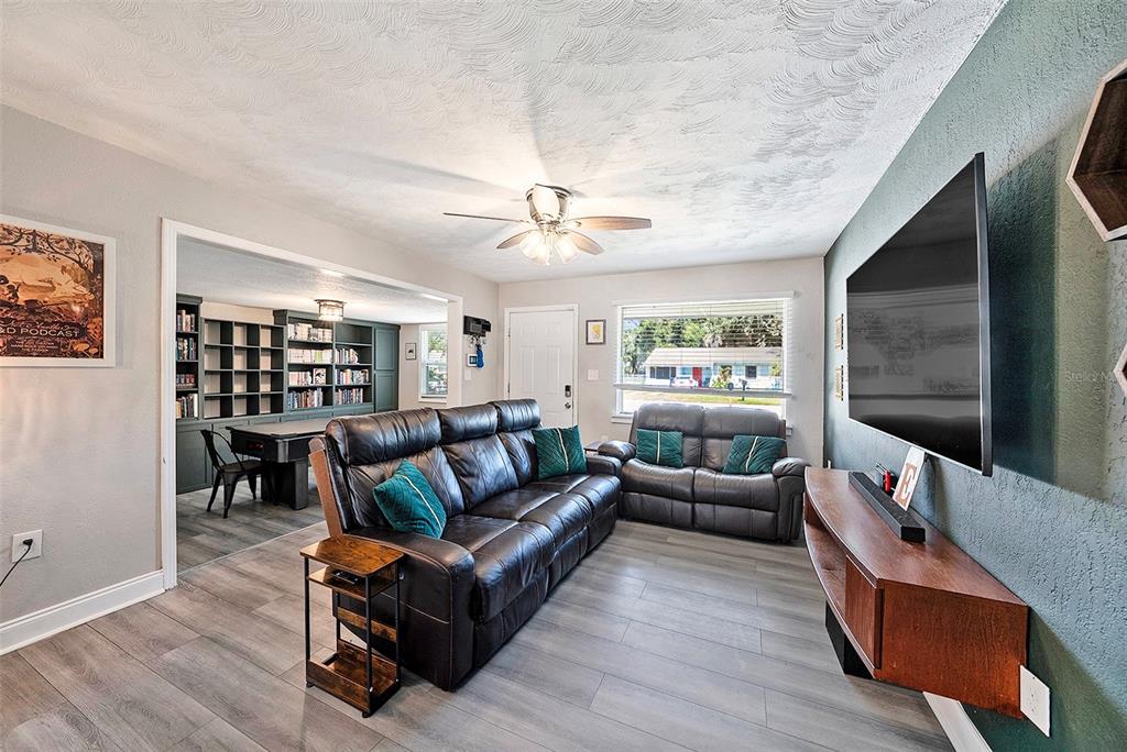 A living room features gray wood-look flooring, a dark accent wall, and a leather sofa — 1209 E FLORA STREET, TAMPA, FL