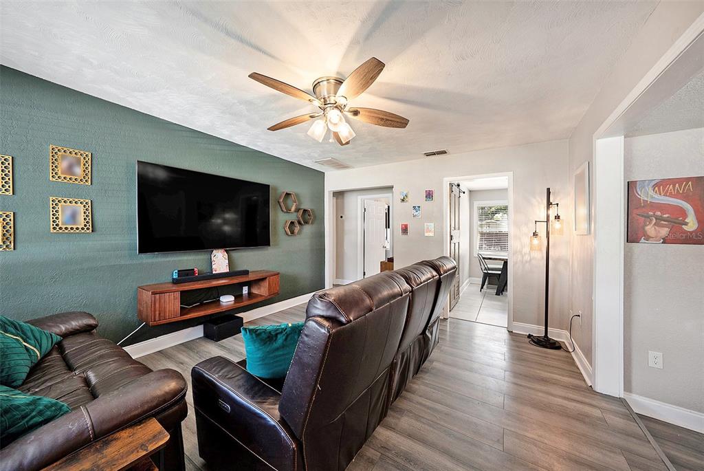 A living room features a green accent wall, a wall-mounted television, and brown leather furniture — 1209 E FLORA STREET, TAMPA, FL