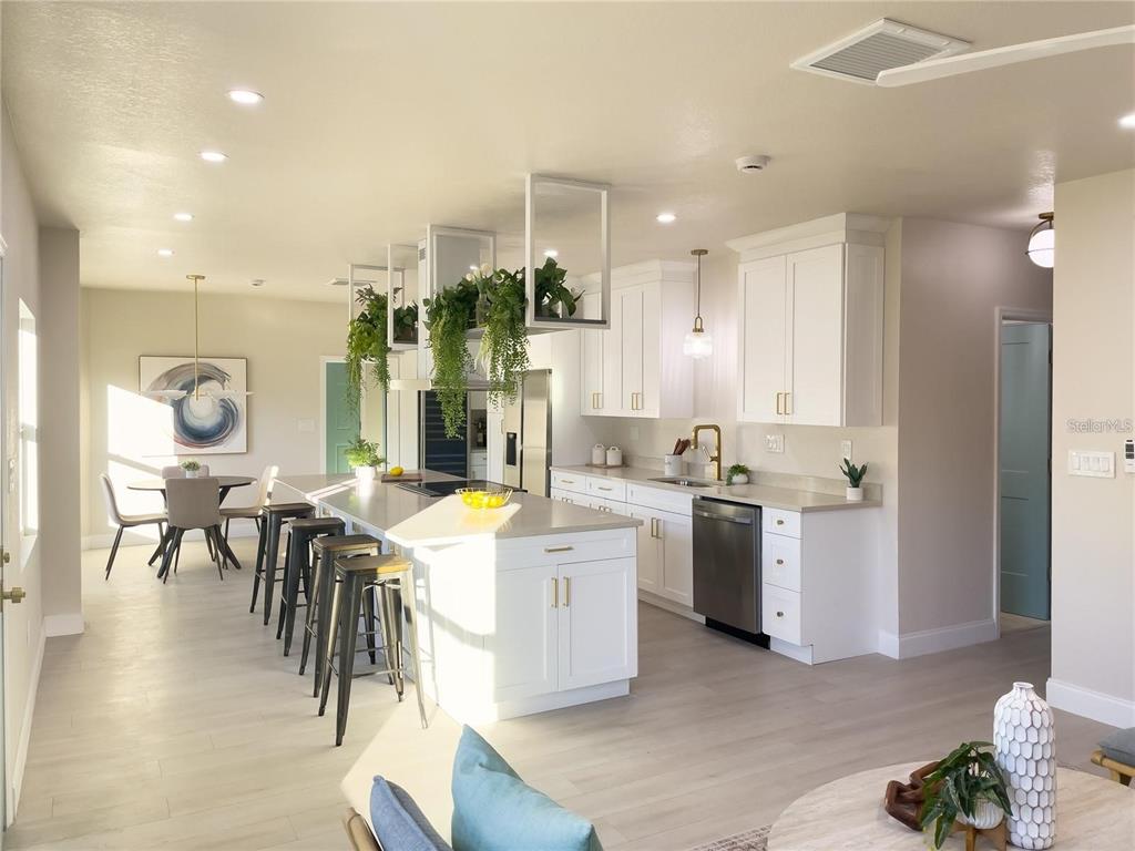 A bright, modern kitchen features white cabinetry, a large central island with barstools, and greenery — 5516 GOLDEN DRIVE, TAMPA, FL