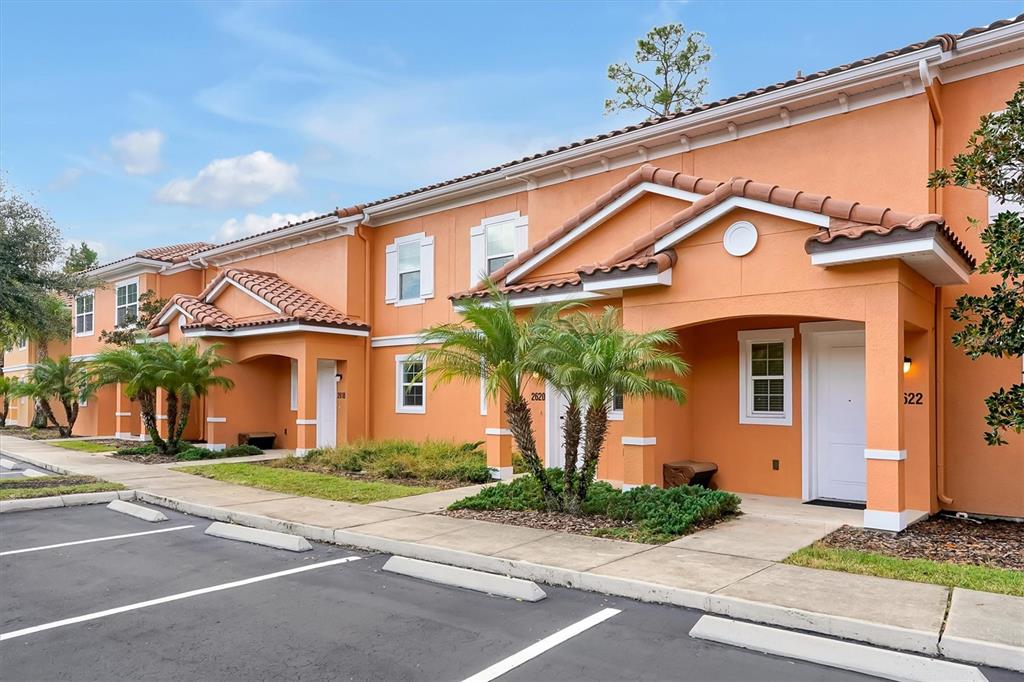 An exterior view of a two-story orange stucco apartment building with a parking lot — 2622 BUGATTI COURT, KISSIMMEE, FL