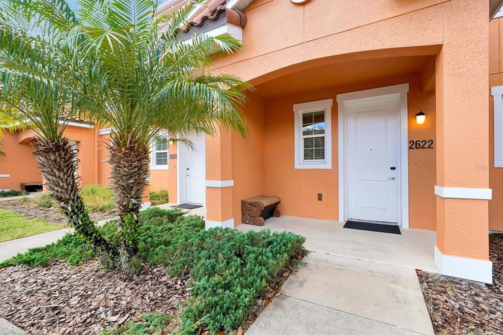 The exterior of a peach-colored townhouse features a white front door and a palm tree — 2622 BUGATTI COURT, KISSIMMEE, FL