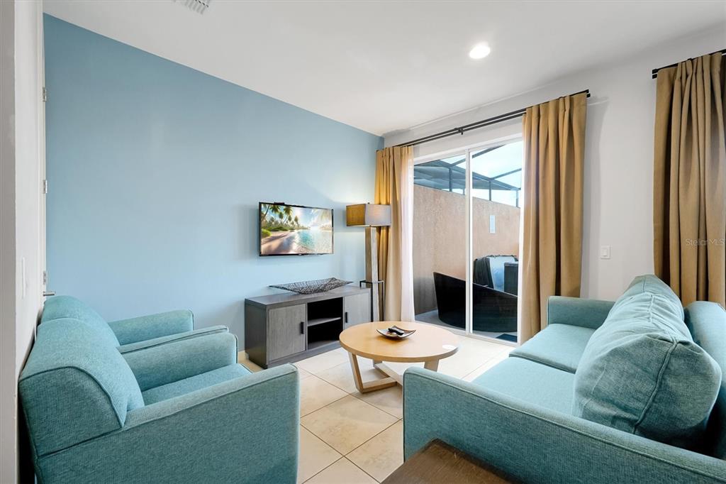 A living room features teal sofas, a light blue accent wall, and a sliding glass door — 2622 BUGATTI COURT, KISSIMMEE, FL