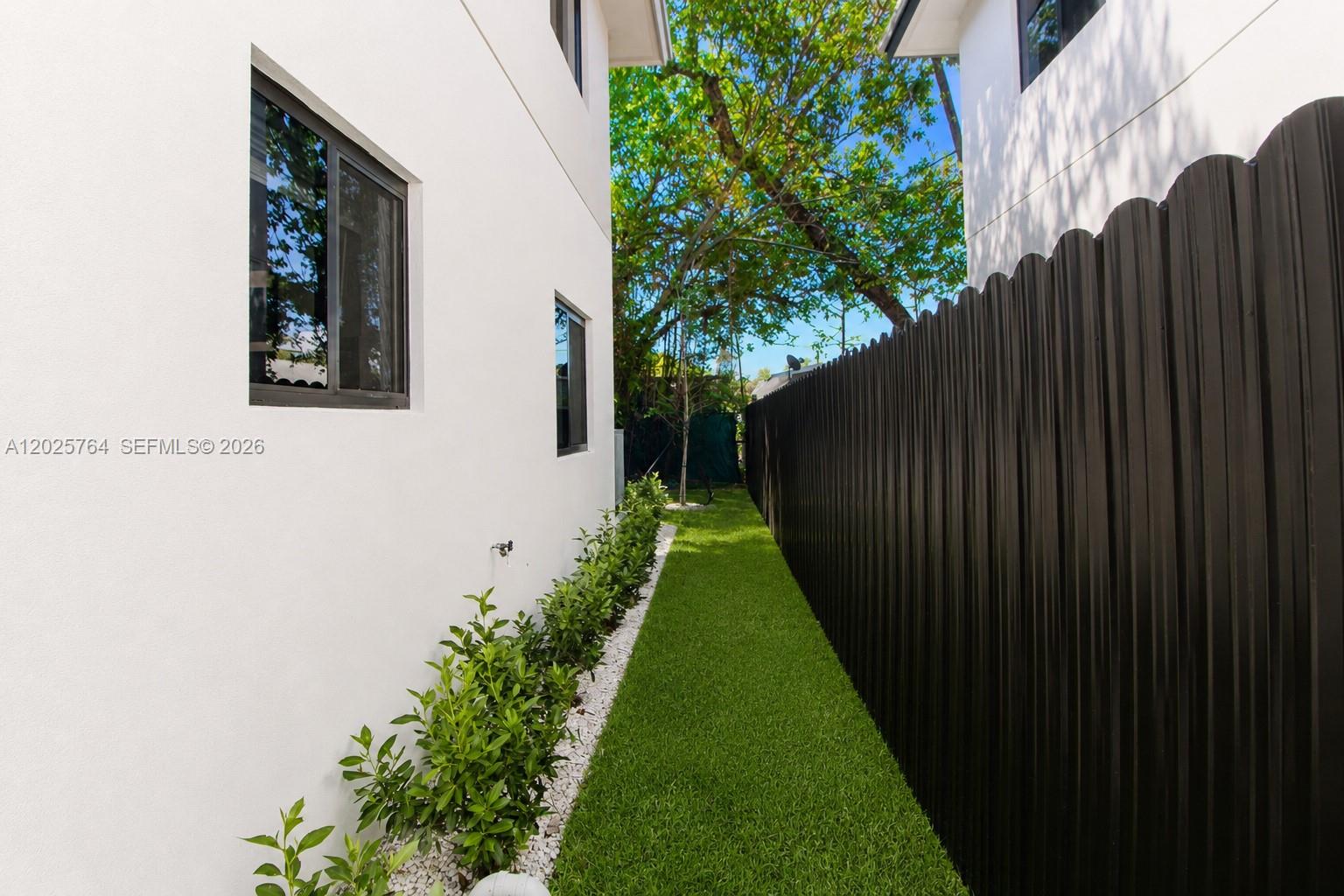 A narrow side yard features artificial turf, a white wall, and a black metal fence — 1836 NW 63rd St # 1836, Miami FL 33147, MIAMI, FL