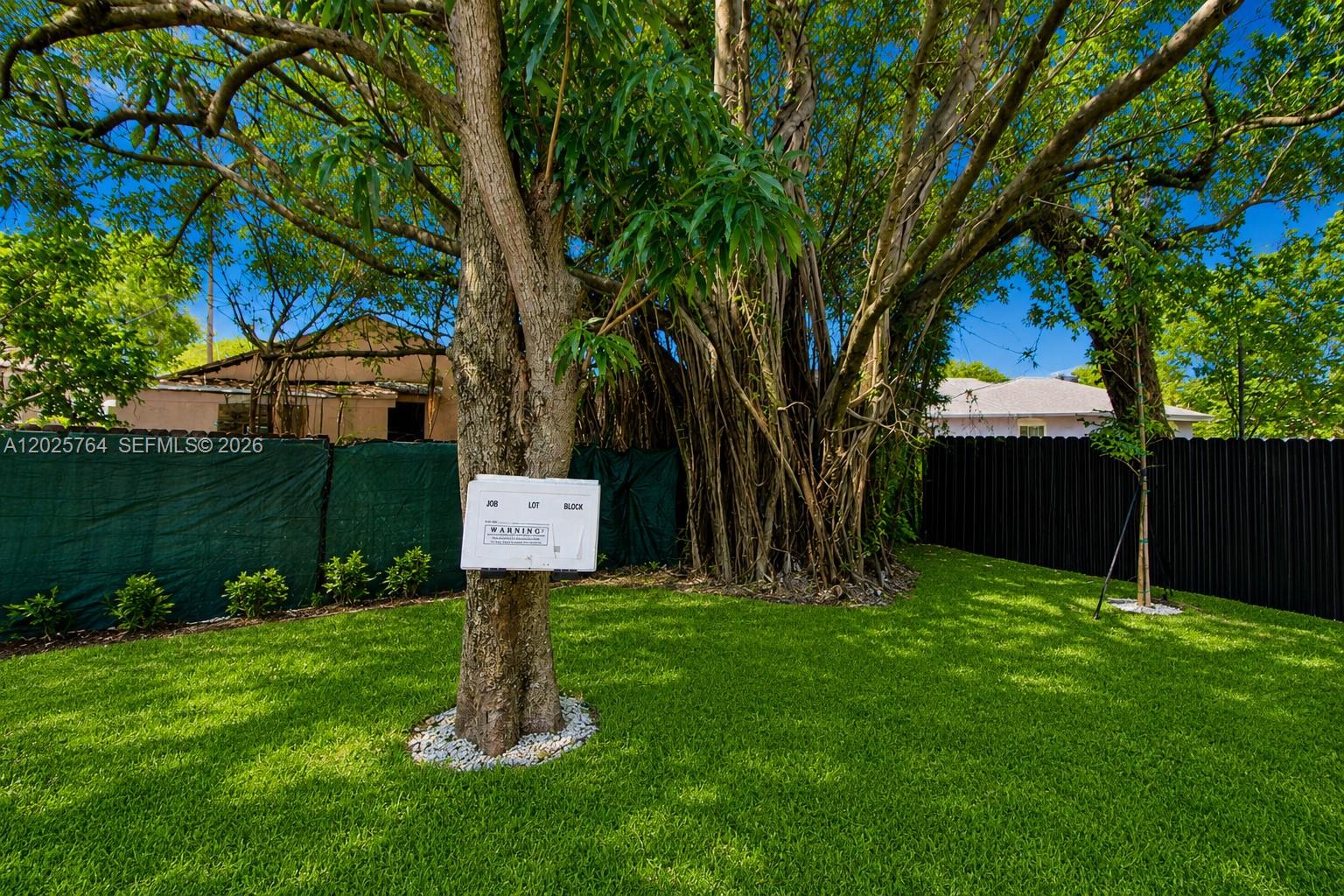 A grassy backyard features a large tree with a permit sign and a privacy fence — 1836 NW 63rd St # 1836, Miami FL 33147, MIAMI, FL