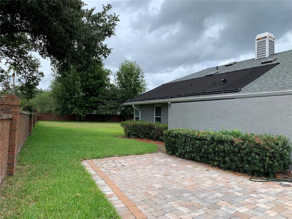 A backyard features a brick-paved patio, a grassy lawn, and a house with solar panels — 434 SILVER DEW STREET, LAKE MARY, FL