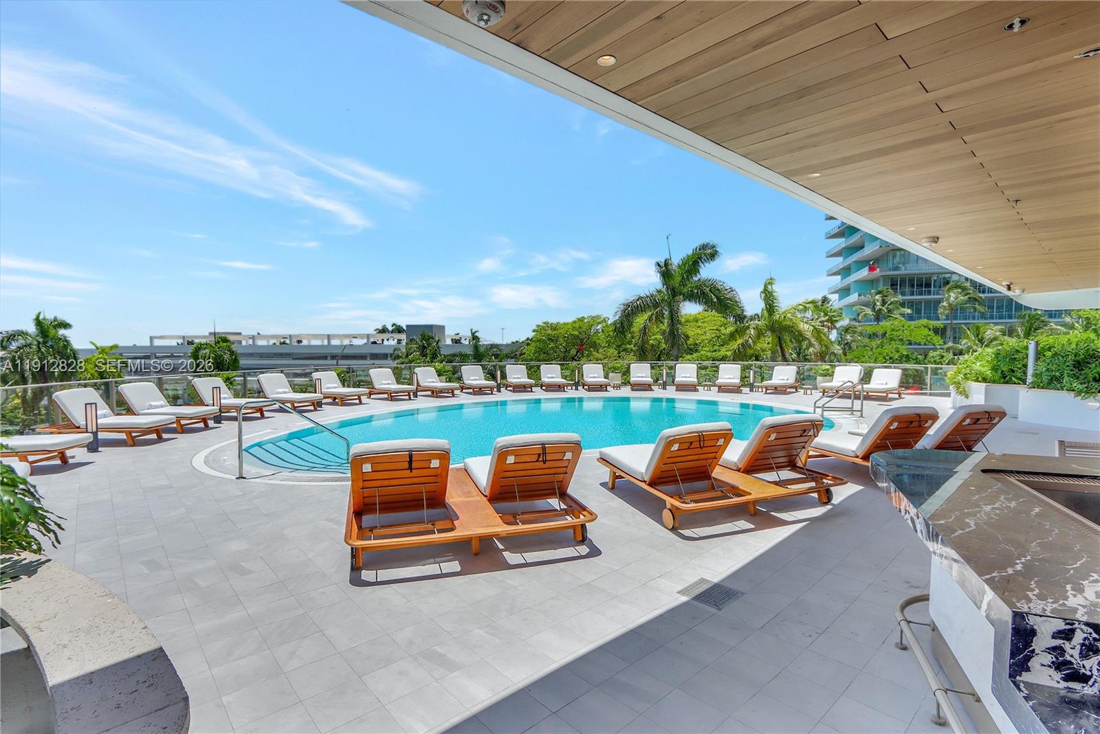A swimming pool surrounded by lounge chairs on a paved deck under a covered patio — 2655 S Bayshore Dr # 405, Miami FL 33133, MIAMI, FL