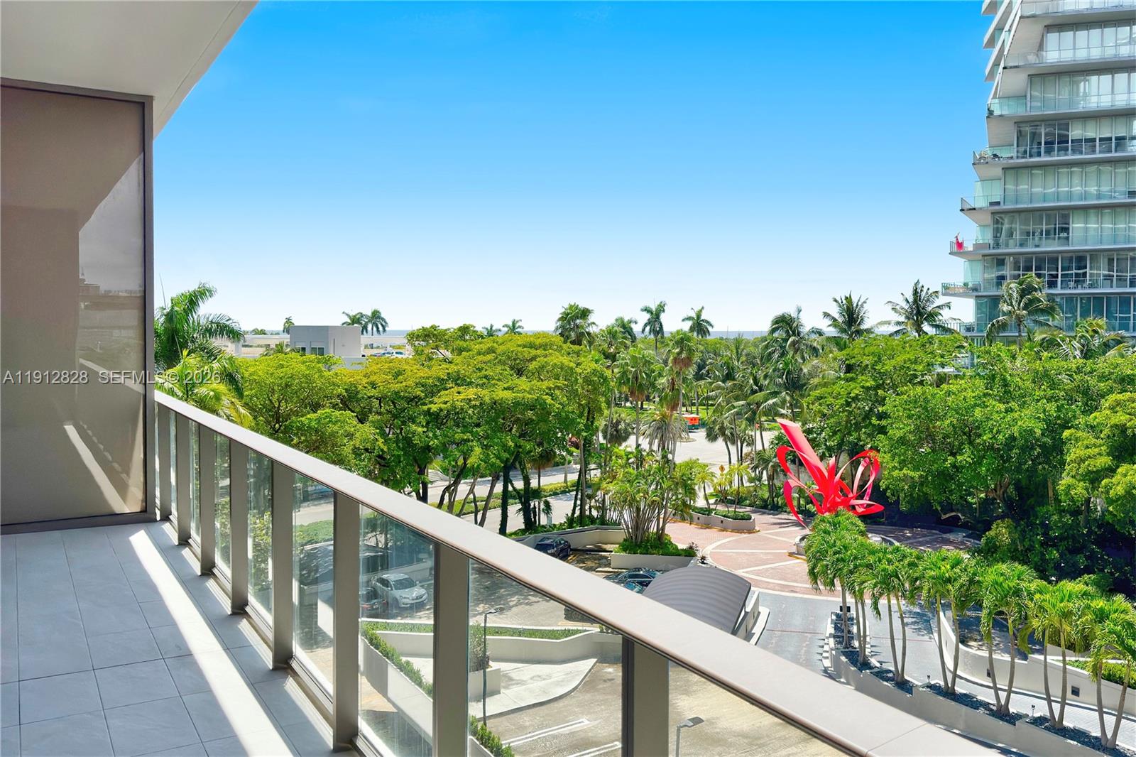 A balcony with a glass railing overlooks a park with trees and a red sculpture — 2655 S Bayshore Dr # 405, Miami FL 33133, MIAMI, FL