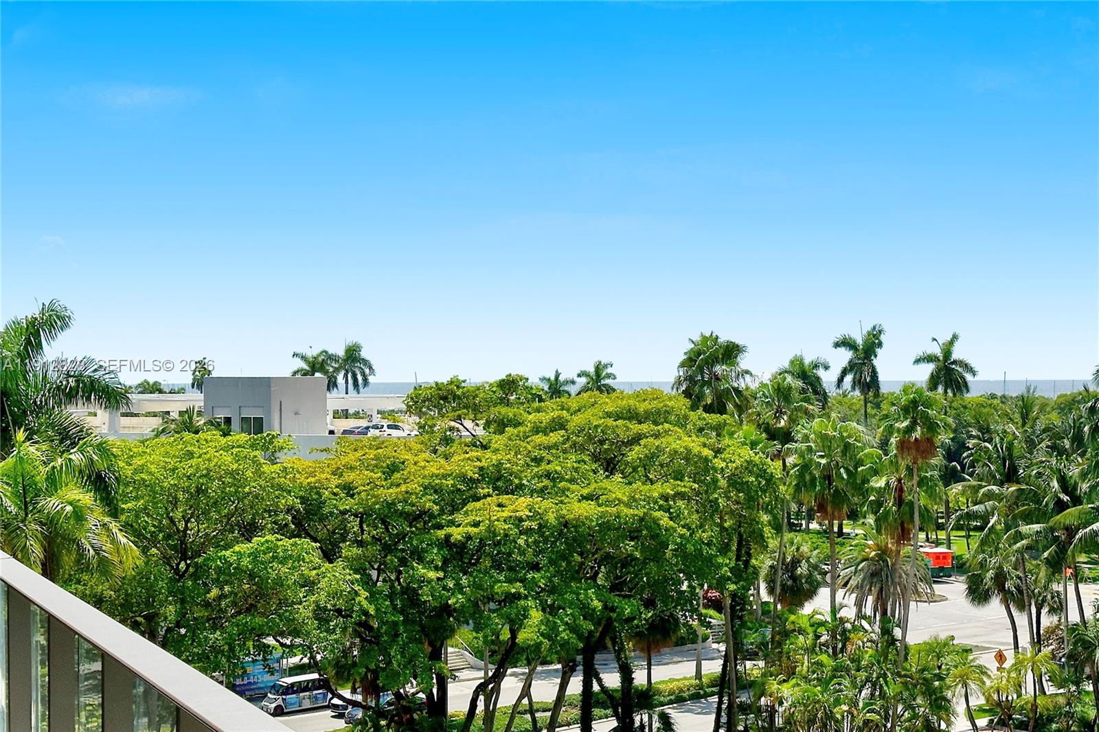 A view from a balcony overlooking a parking lot, lush green trees, and the ocean — 2655 S Bayshore Dr # 405, Miami FL 33133, MIAMI, FL
