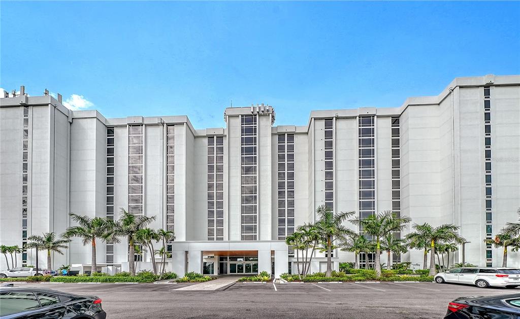 A multi-story white apartment building features vertical glass windows and palm trees in the foreground — 2425 GULF OF MEXICO DRIVE UNIT 3A, LONGBOAT KEY, FL