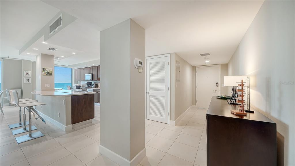 A modern kitchen with a breakfast bar overlooks the ocean, adjacent to an entryway hallway — 2425 GULF OF MEXICO DRIVE UNIT 3A, LONGBOAT KEY, FL