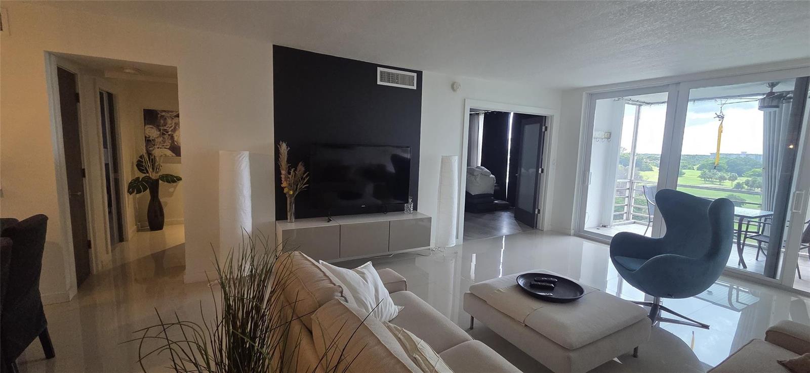 A modern living room features a black accent wall, tile flooring, and a balcony view — 2671 S Course Drive # 806, Pompano Beach FL 33069, POMPANO BEACH, FL