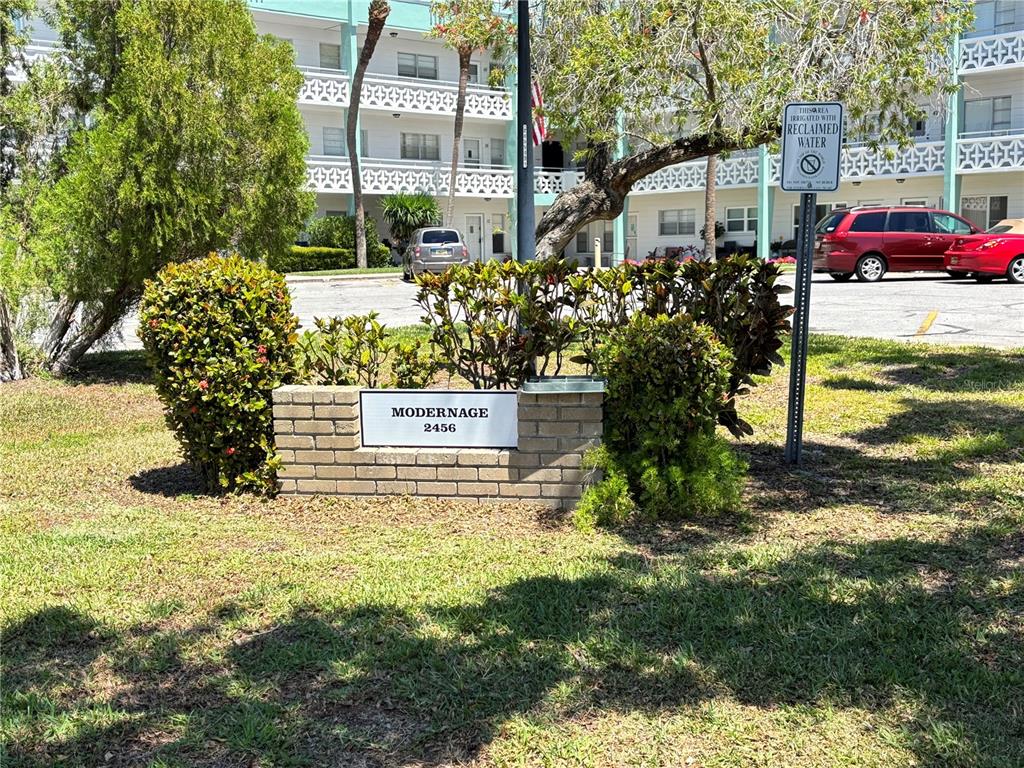 A brick sign for the Modernage complex stands in front of a multi-story apartment building — 2456 ECUADORIAN WAY UNIT 42, CLEARWATER, FL