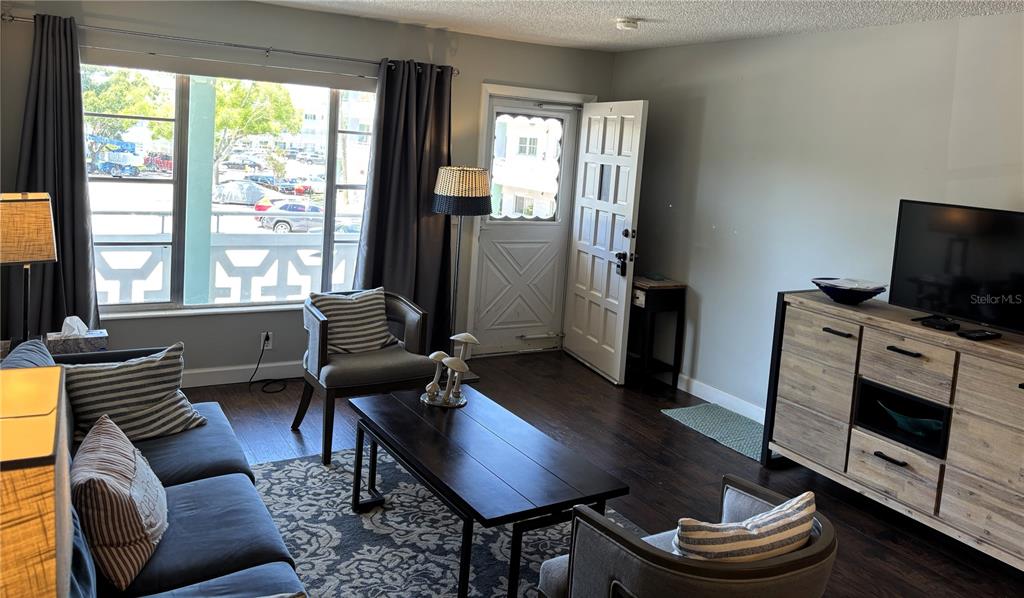 A living room features dark wood floors, a large window, and a television on a dresser — 2456 ECUADORIAN WAY UNIT 42, CLEARWATER, FL