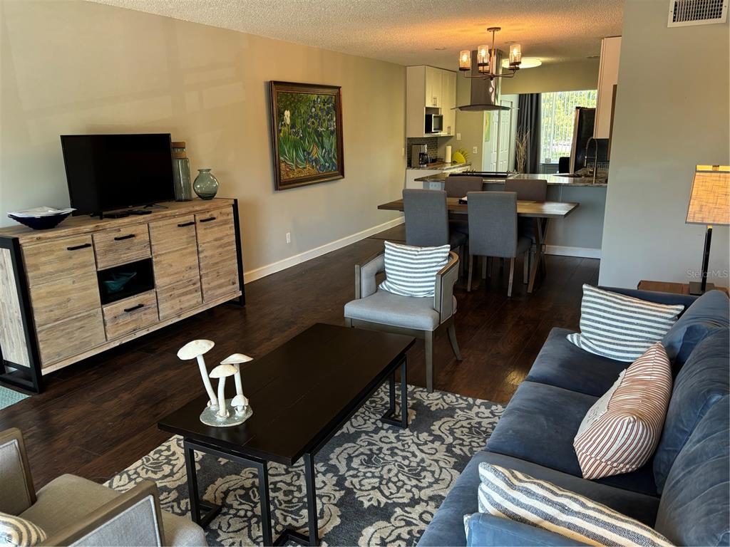 A living room with dark wood floors flows into an open kitchen and dining area — 2456 ECUADORIAN WAY UNIT 42, CLEARWATER, FL