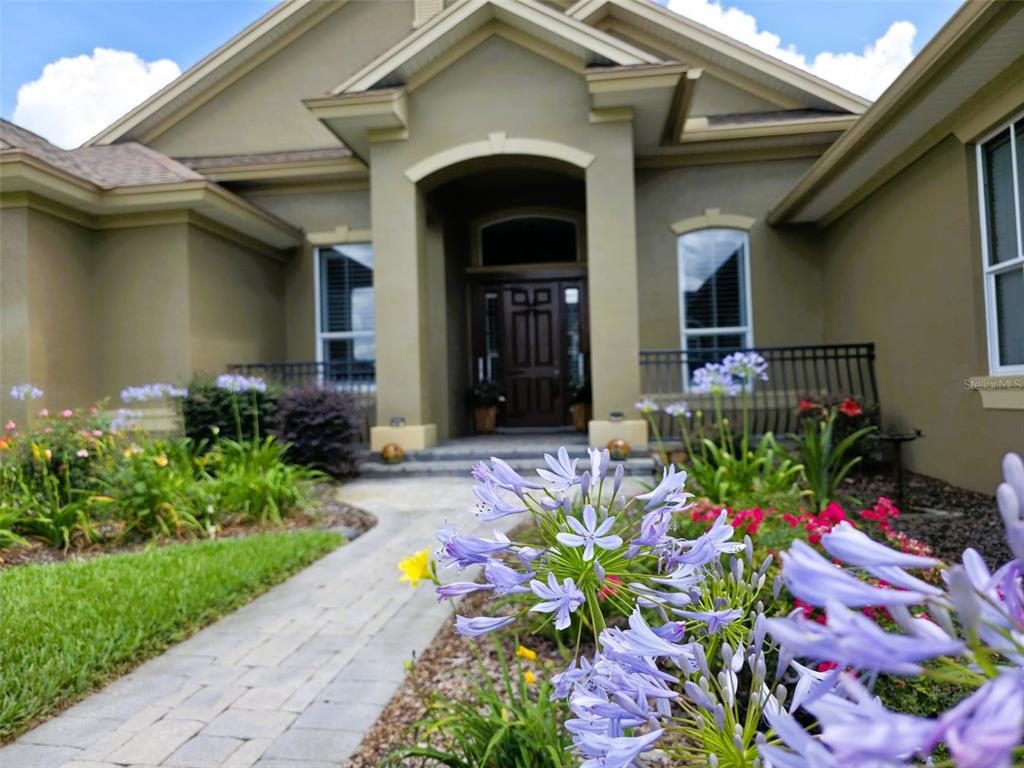 A paved walkway leads to the front entrance of a tan house with purple flowers — 5629 HILLSIDE LANDINGS ROAD, LAKELAND, FL