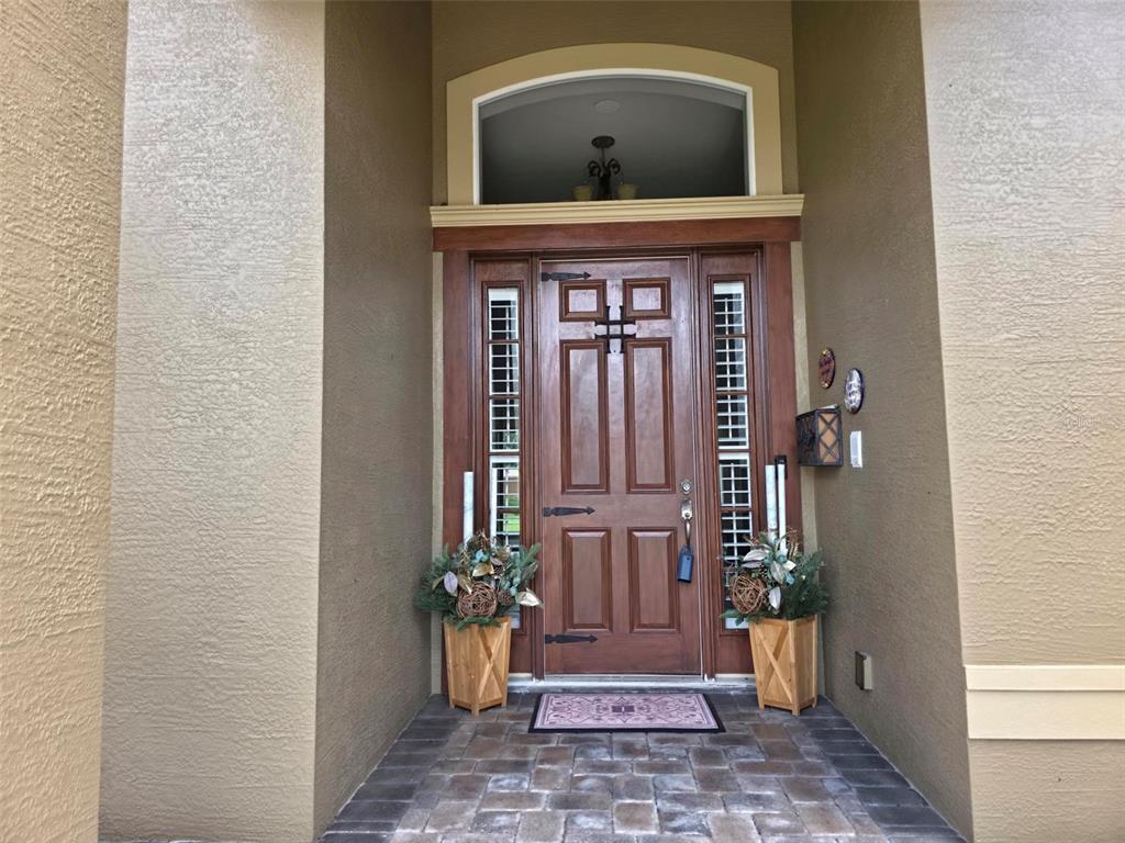 A wooden front door with sidelights and a transom window sits under a covered entryway — 5629 HILLSIDE LANDINGS ROAD, LAKELAND, FL