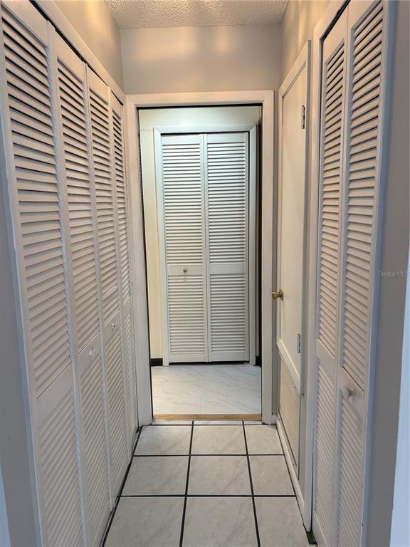 A hallway features white louvered closet doors on both sides and light-colored tile flooring — 671 OLYMPIC DRIVE UNIT 16-4, OCOEE, FL