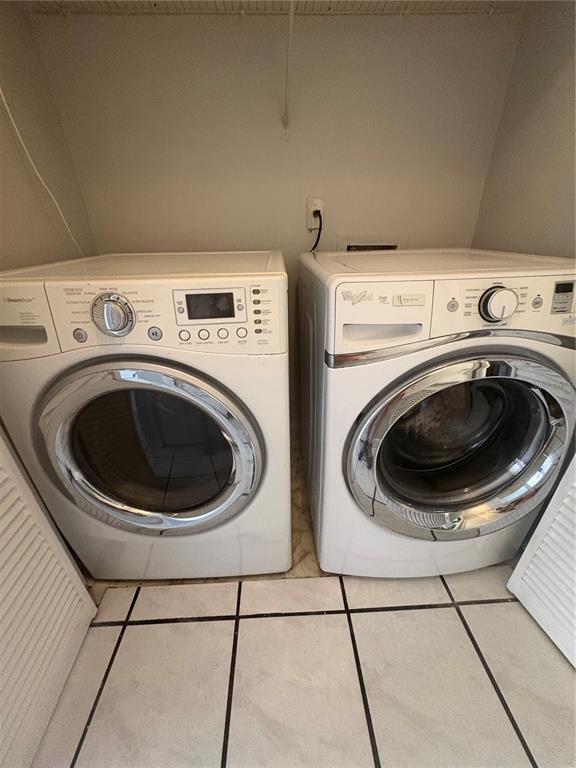 A laundry closet contains a white front-loading washer and dryer on a tiled floor — 671 OLYMPIC DRIVE UNIT 16-4, OCOEE, FL