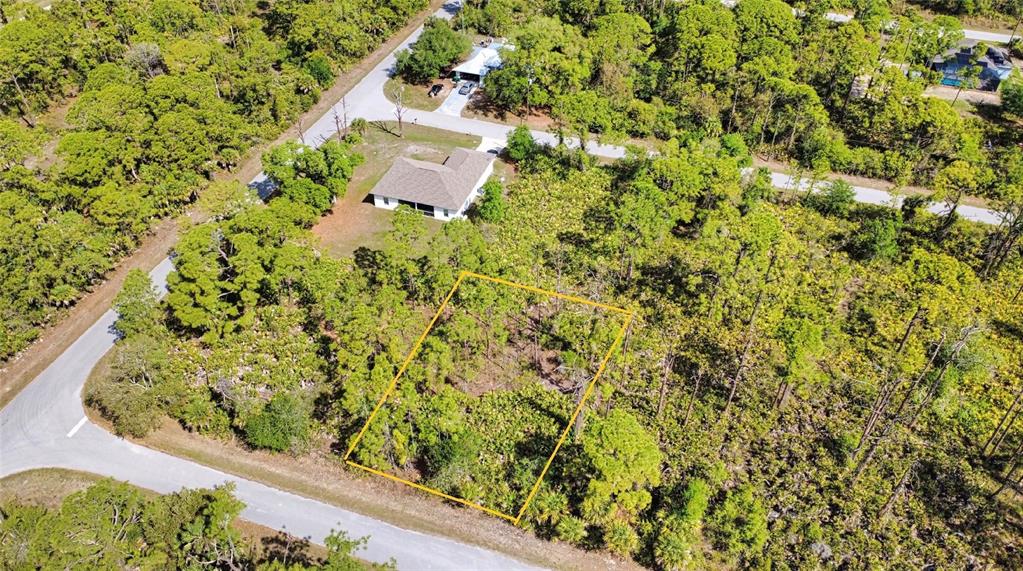 An aerial view shows a vacant, wooded lot outlined in yellow near a residential house — 13312 HARTH AVENUE, PORT CHARLOTTE, FL