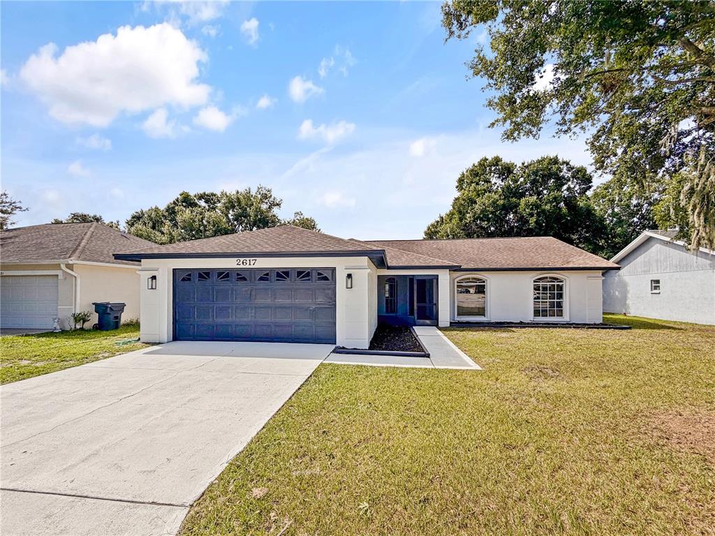 A single-story house with a dark garage door, white exterior walls, and a paved driveway — 2617 SUNDANCE CIRCLE, MULBERRY, FL