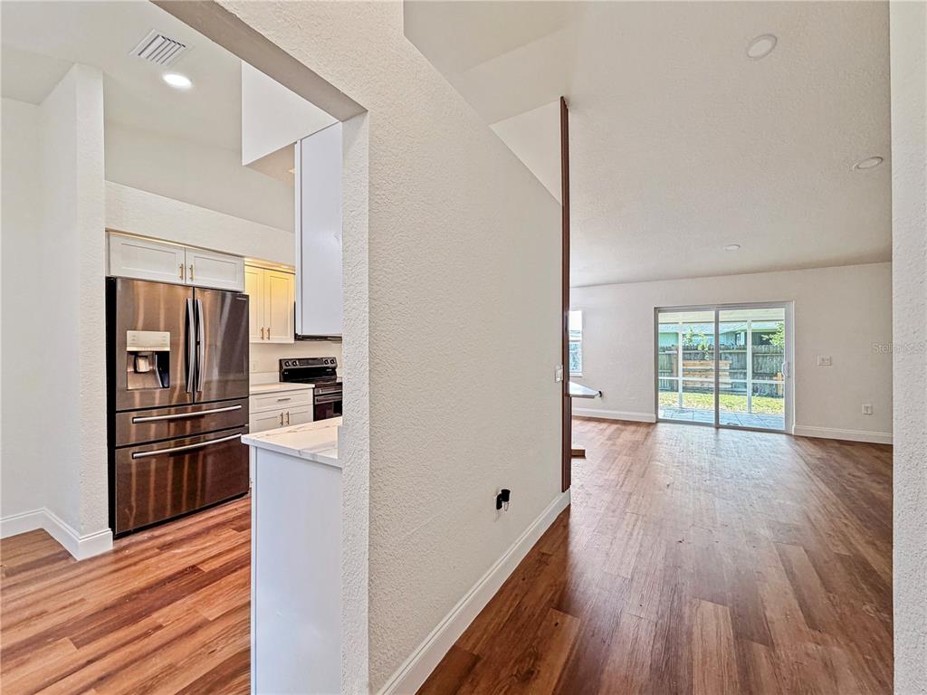 A view from a kitchen into an open living area with wood-look flooring and sliding doors — 2617 SUNDANCE CIRCLE, MULBERRY, FL