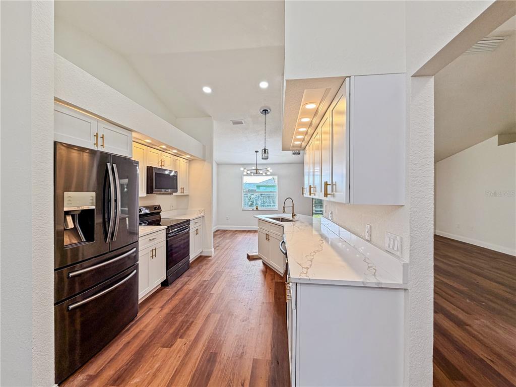 A kitchen with white cabinets, dark appliances, and wood-look flooring leads to a dining area — 2617 SUNDANCE CIRCLE, MULBERRY, FL