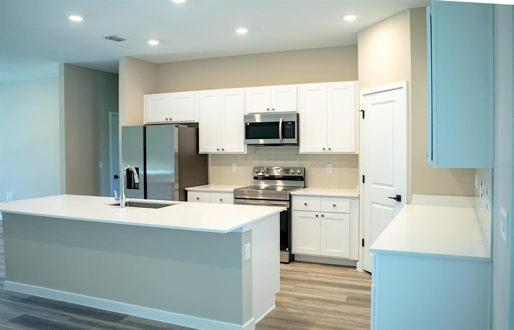 A modern kitchen features white cabinets, stainless steel appliances, and a large central island — 5 SERVICE BERRY PLACE, PALM COAST, FL