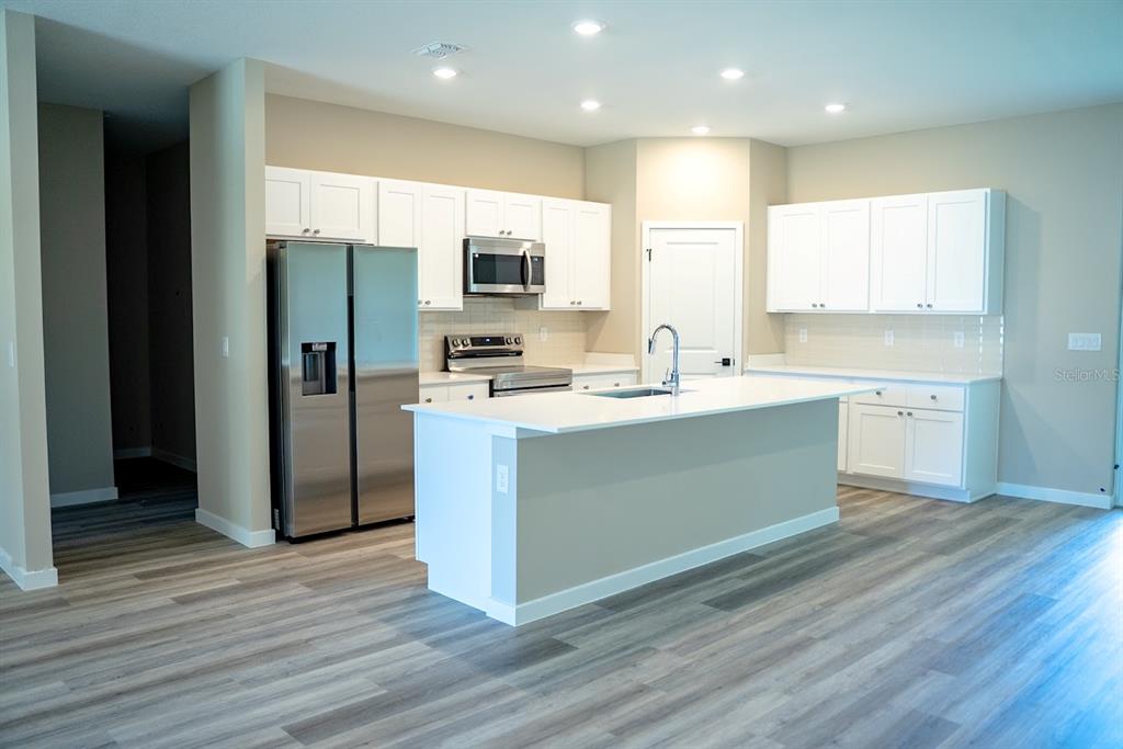 A modern kitchen features white cabinets, stainless steel appliances, a center island, and wood-look flooring — 5 SERVICE BERRY PLACE, PALM COAST, FL