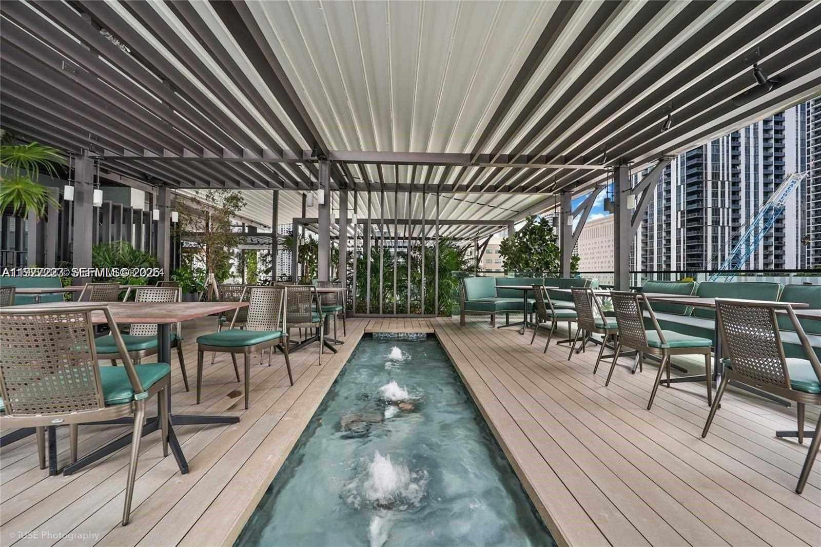 An outdoor patio features a central water feature, wooden decking, and modern dining furniture — 159 NE 6th St # 4113, Miami FL 33132, MIAMI, FL