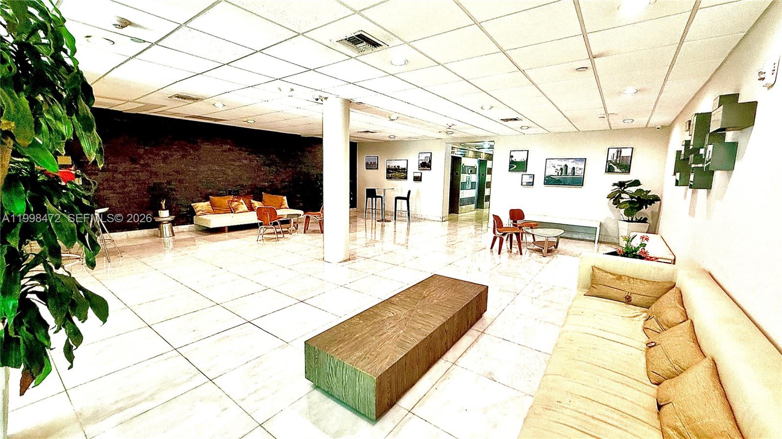 A spacious, tiled lobby features a long sofa, a central wooden bench, and wall art — 1035 West Ave # 306, Miami Beach FL 33139, MIAMI BEACH, FL