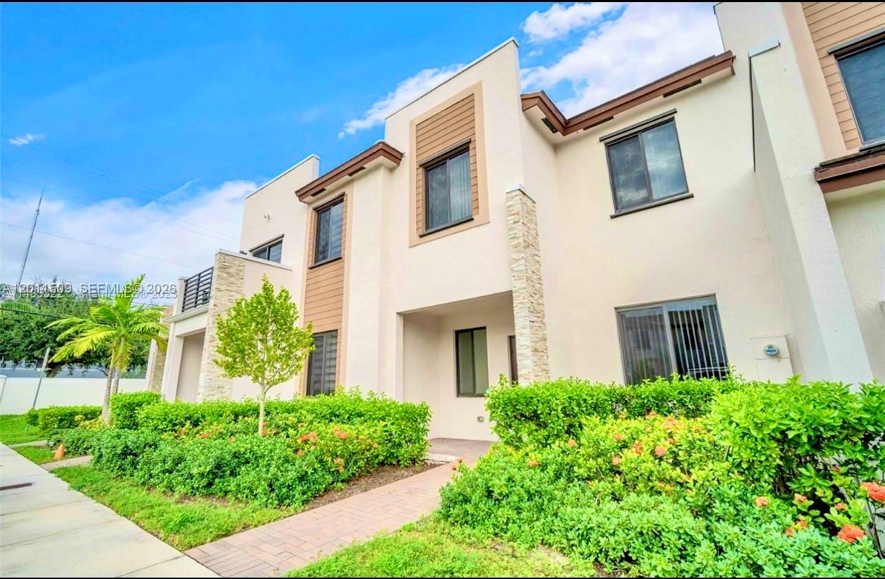 A two-story townhouse exterior features beige stucco walls, stone accents, and a paved walkway — 21443 NE 2nd Path # 21443, Miami FL 33179, MIAMI, FL