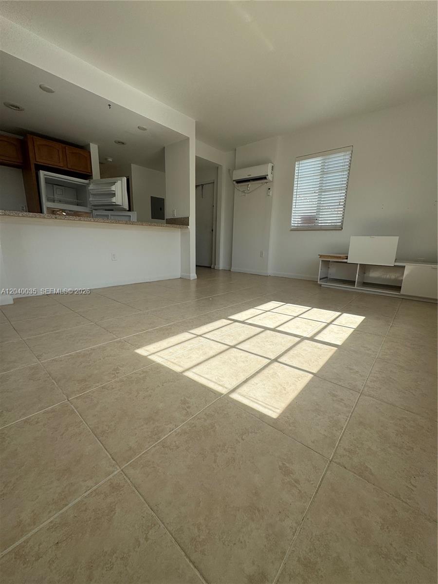 An open-concept living area features light-colored floor tiles, a kitchen pass-through, and a wall-mounted air conditioner — 7130 Rue Versailles # 11, Miami Beach FL 33141, MIAMI BEACH, FL