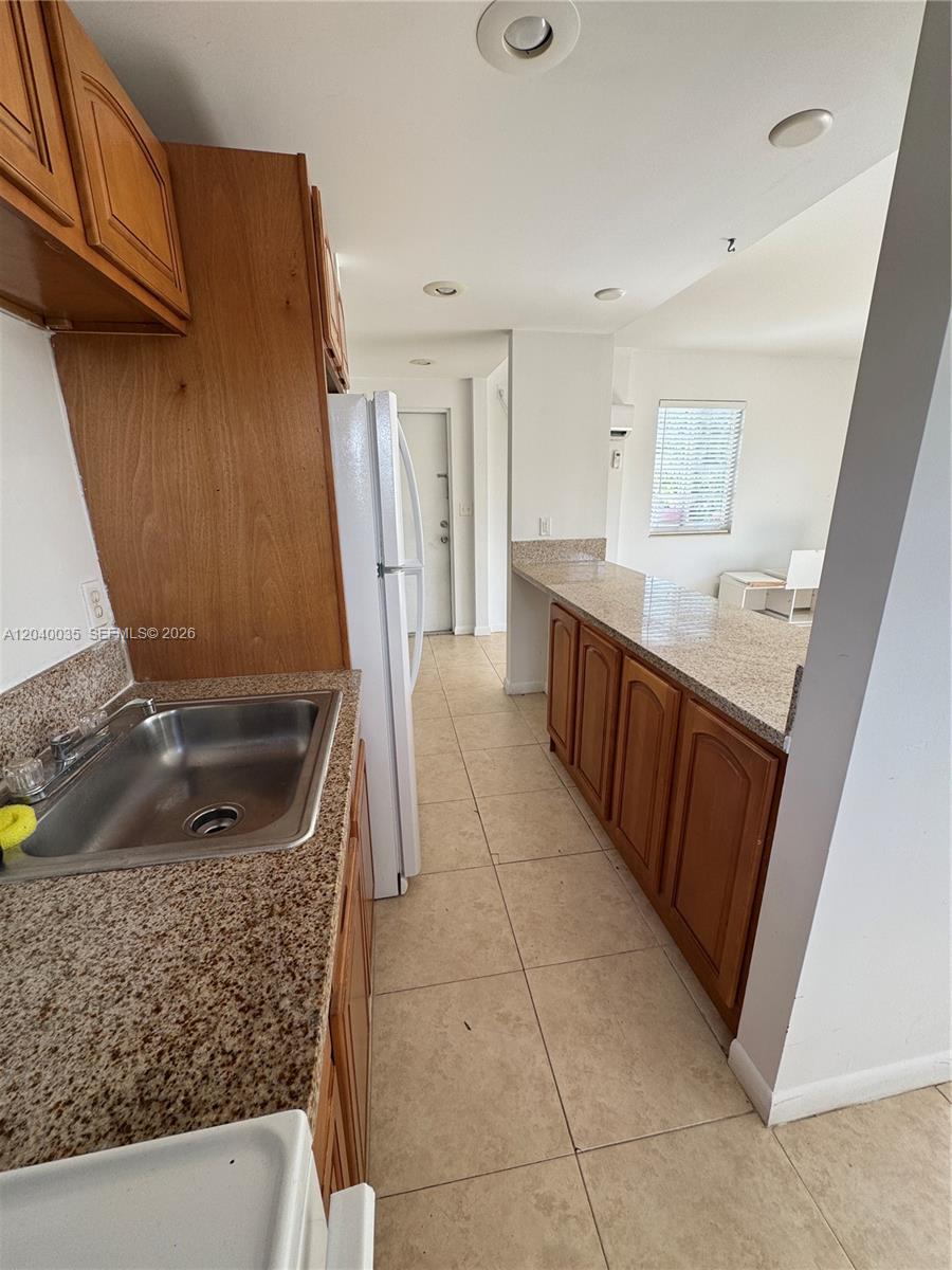 A kitchen features wood cabinets, granite countertops, a stainless steel sink, and tile flooring — 7130 Rue Versailles # 11, Miami Beach FL 33141, MIAMI BEACH, FL