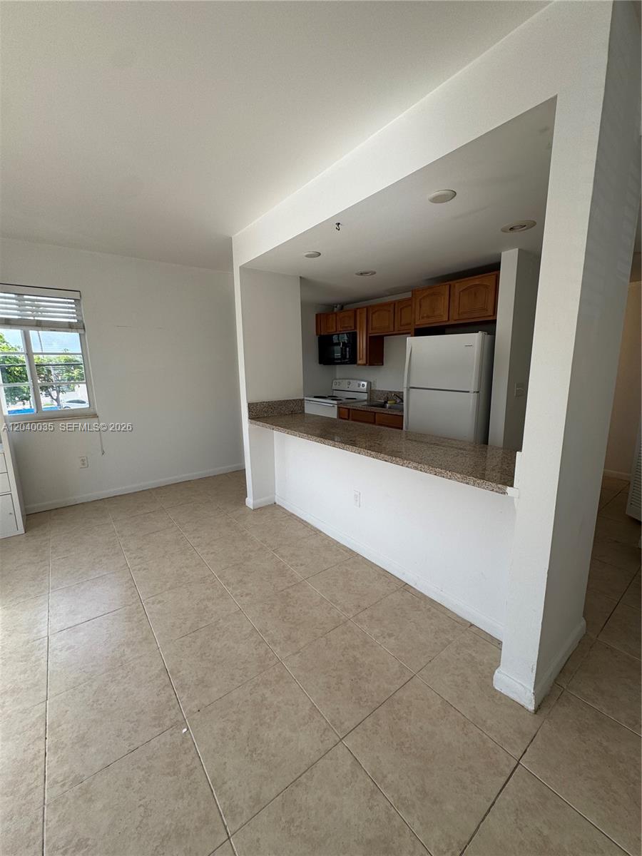 A kitchen with wood cabinets and a granite breakfast bar overlooks a tiled living area — 7130 Rue Versailles # 11, Miami Beach FL 33141, MIAMI BEACH, FL