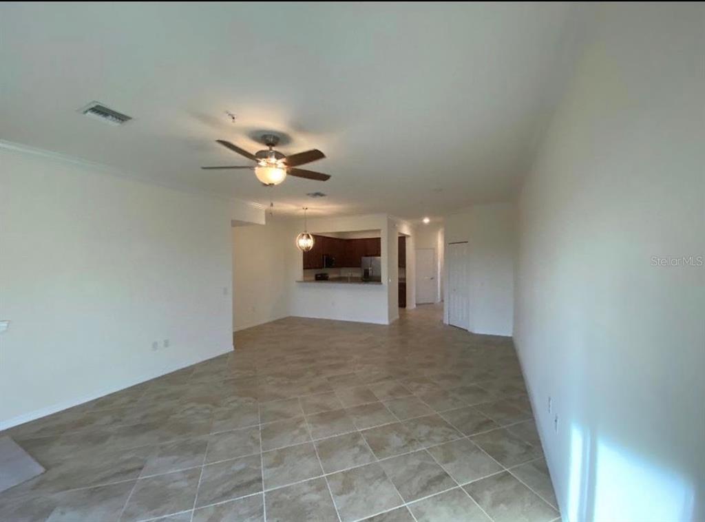 An open-concept living area features light-colored tile flooring, a ceiling fan, and a kitchen pass-through — 20270 LA GENTE CIRCLE, VENICE, FL
