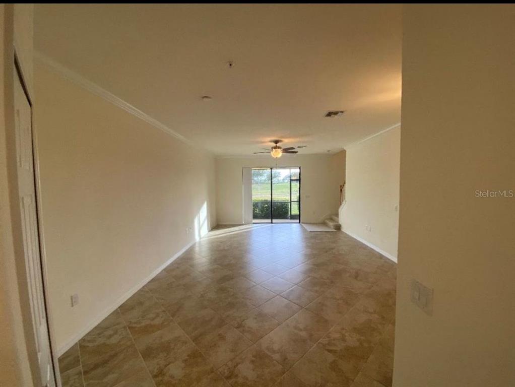 An empty living room with beige tile flooring and a sliding glass door to the outside — 20270 LA GENTE CIRCLE, VENICE, FL