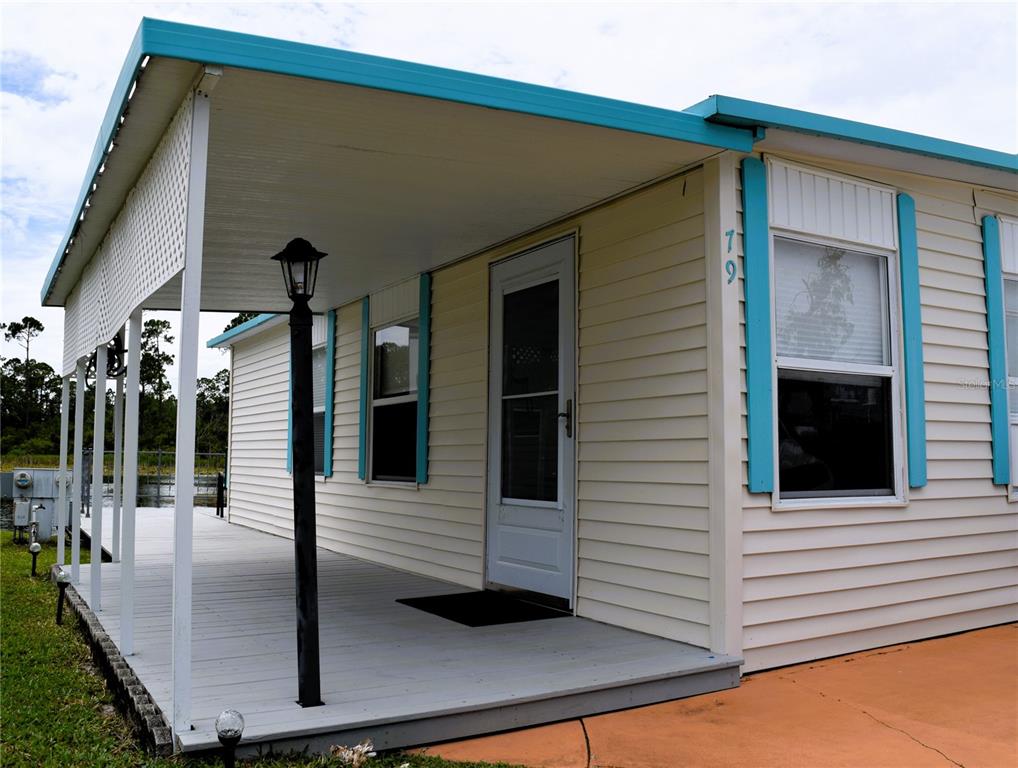 A mobile home exterior features light siding, blue trim, a covered porch, and a front door — 79 EAGLE POINT S, OSTEEN, FL