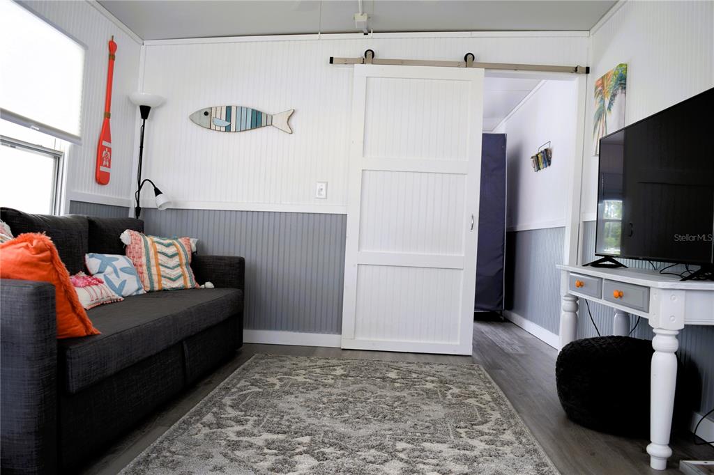 A living room features a gray sofa, a white barn door, and a television on console — 79 EAGLE POINT S, OSTEEN, FL