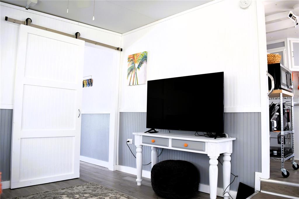 A living room features a white barn door, a television on a console, and wainscoting — 79 EAGLE POINT S, OSTEEN, FL