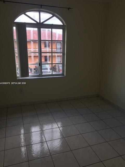 An empty room with light-colored tile flooring and an arched window overlooking an apartment building — 655 W 68th St # 4, Hialeah FL 33014, HIALEAH, FL