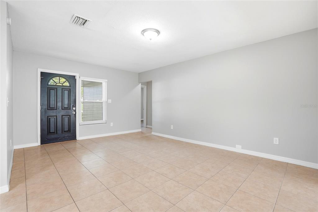 A living room with light gray walls, beige tile flooring, and a dark front door — 301 TERRACE DRIVE E, CLEARWATER, FL