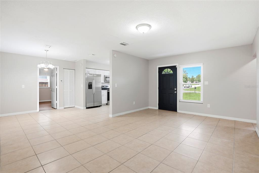 An open-concept living area features light tile flooring, a black front door, and a kitchen — 301 TERRACE DRIVE E, CLEARWATER, FL