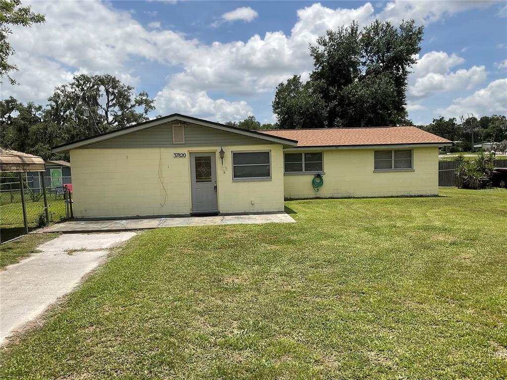 A single-story house with yellow concrete block walls and a brown shingled roof — 37820 CRYSTAL WAY, DADE CITY, FL