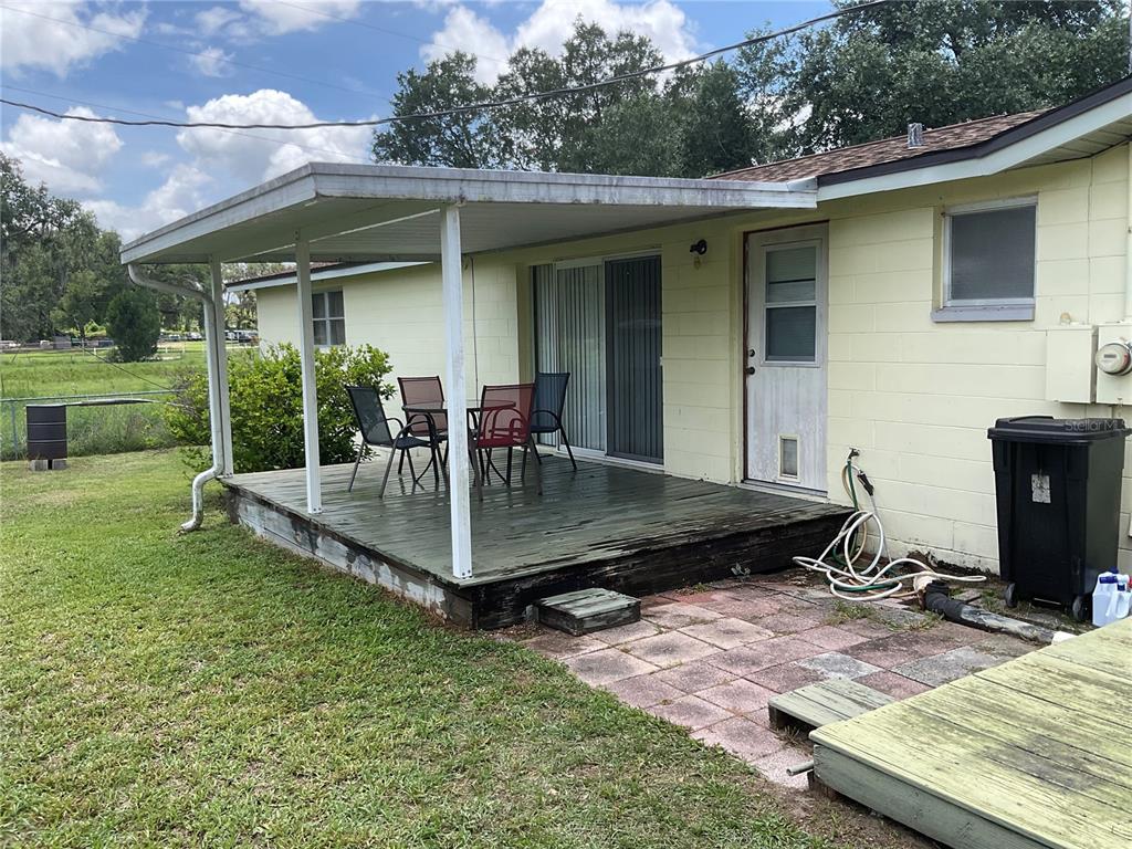 A yellow house features a covered wooden deck with outdoor furniture and a patio area — 37820 CRYSTAL WAY, DADE CITY, FL