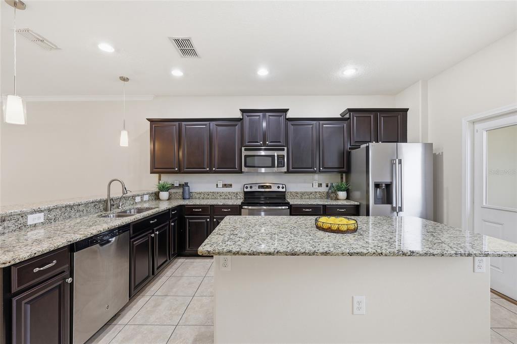 A kitchen features dark wood cabinets, granite countertops, stainless steel appliances, and a central island — 1351 VASEY ROAD, APOPKA, FL