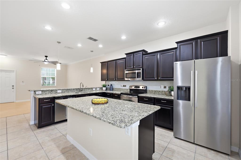 A kitchen features dark wood cabinets, granite countertops, a center island, and stainless steel appliances — 1351 VASEY ROAD, APOPKA, FL